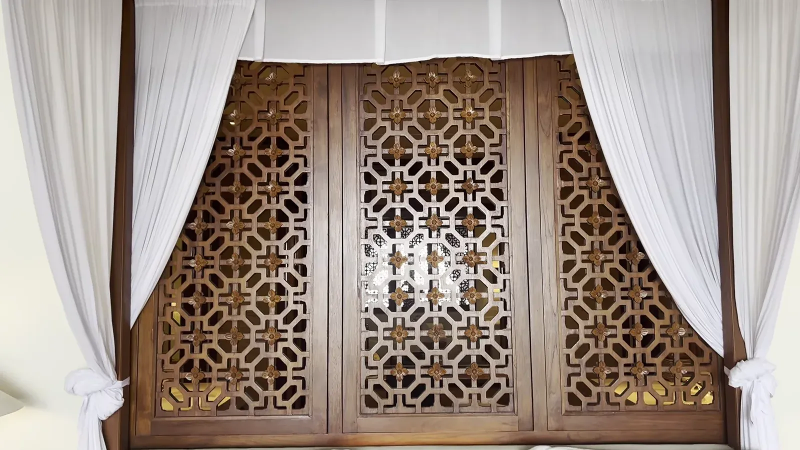 The bedroom at The Sira Lombok behind a carved teak screen and white curtains